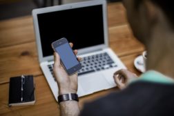 Man holds smart phone in front of computer