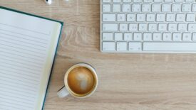 desk with coffee, keyboard and notebook