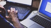 person working at two laptops