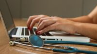 person using laptop next to stethoscope 