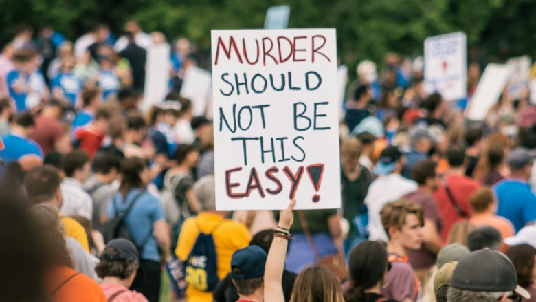Person in crowd holding gun safety sign