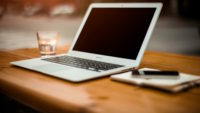 Laptop open on wooden desk with notebook