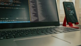 Computer open on desk beside cell phone