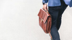 Person in blue pants and jacket carrying brown briefcase